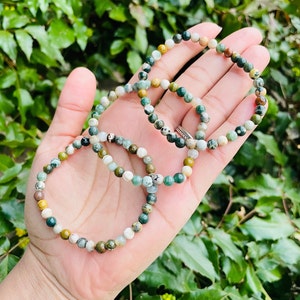 May include: Three green, brown, and white gemstone bracelets stacked on a hand. The bracelets are made of small, round beads.