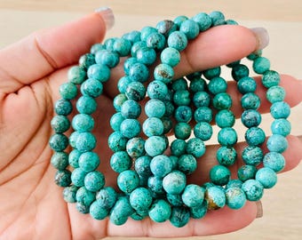 May include: A stack of turquoise gemstone bracelets with round beads. The bracelets are made of natural turquoise stones with a mottled green and blue color.