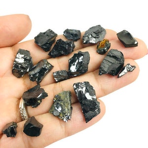 May include: A collection of black, raw, and unpolished pieces of black tourmaline crystals. The crystals are various sizes and shapes, and some have a slight sheen.