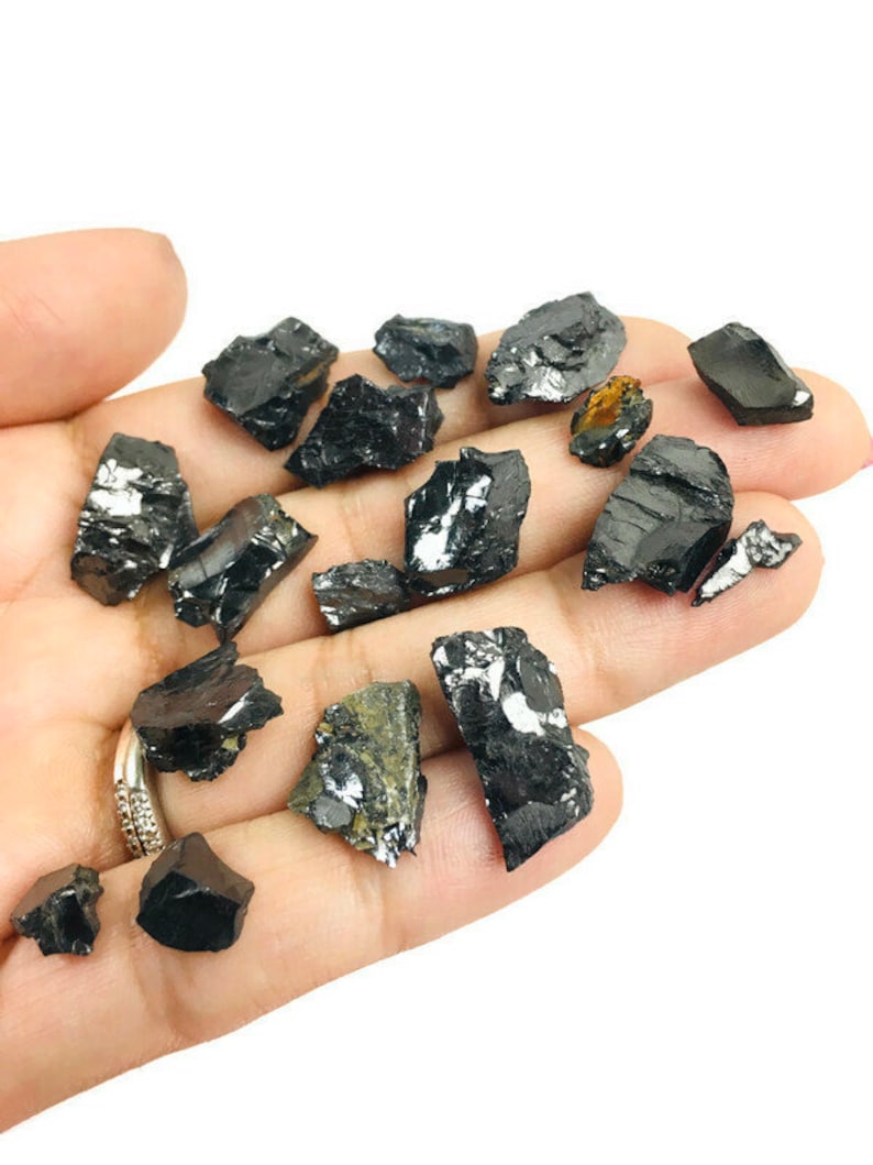 May include: A collection of black, raw, and unpolished pieces of black tourmaline crystals. The crystals are various sizes and shapes, and some have a slight sheen.