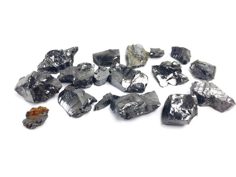 May include: A collection of black, shiny, irregularly shaped, rough-edged, natural mineral stones on a white background.