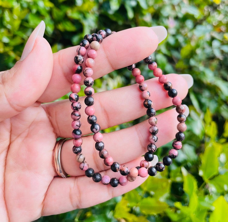 May include: Two pink and black gemstone bracelets with small round beads.