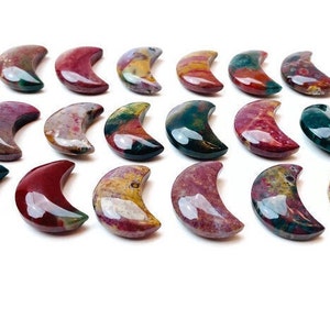 May include: A collection of 18 polished, multi-colored, crescent moon shaped stones. The stones are a mix of red, green, yellow, and brown.