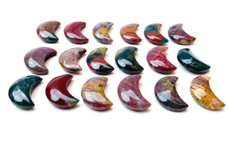 May include: A collection of 18 polished, multi-colored, crescent moon shaped stones. The stones are a mix of red, green, yellow, and brown.