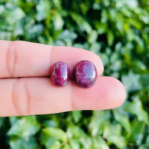 May include: Two round, cabochon-cut ruby gemstones. The stones are a deep red color with a slight purple hue. They are both about the same size and have a smooth, polished finish.