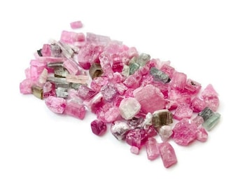 May include: A collection of pink, green, and white tourmaline crystals. The crystals are various sizes and shapes, and some are translucent.