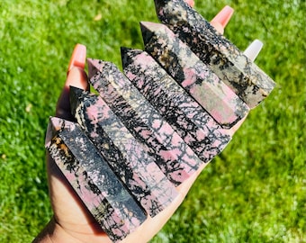 Puede incluir: Una colección de ocho puntas de cristal facetadas pulidas de color rosa y negro. Las puntas están dispuestas en una pila, con la punta más grande en la parte inferior y la punta más pequeña en la parte superior.