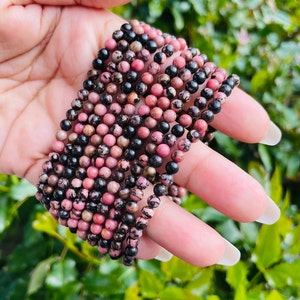 May include: A close-up of a stack of pink and black gemstone beads. The beads are round and have a smooth, polished finish.