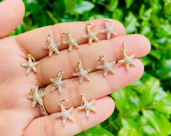 May include: A collection of 11 gold-tone starfish charms with clear crystal accents. The charms are arranged on a hand, with some charms overlapping.