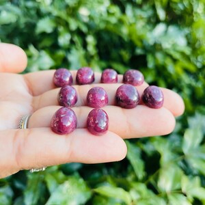 May include: A collection of ten round, cabochon cut, ruby red gemstones. The stones are smooth and polished, with a deep red color.