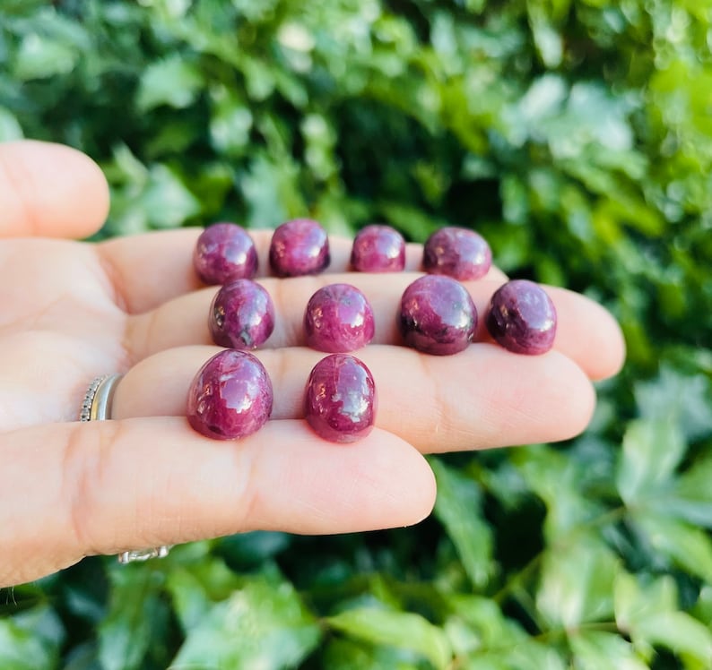 May include: A collection of ten round, cabochon cut, ruby red gemstones. The stones are smooth and polished, with a deep red color.