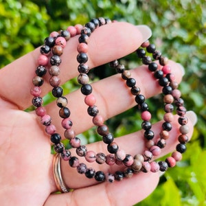 May include: Three layered bracelets made of pink and black gemstone beads. The beads are small and round.