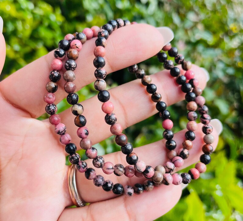 May include: Three layered bracelets made of pink and black gemstone beads. The beads are small and round.