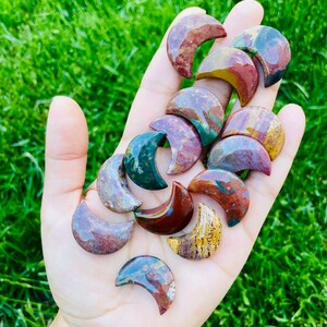 May include: A collection of polished, multi-colored, crescent moon shaped stones. The stones are a mix of red, brown, green, and yellow.