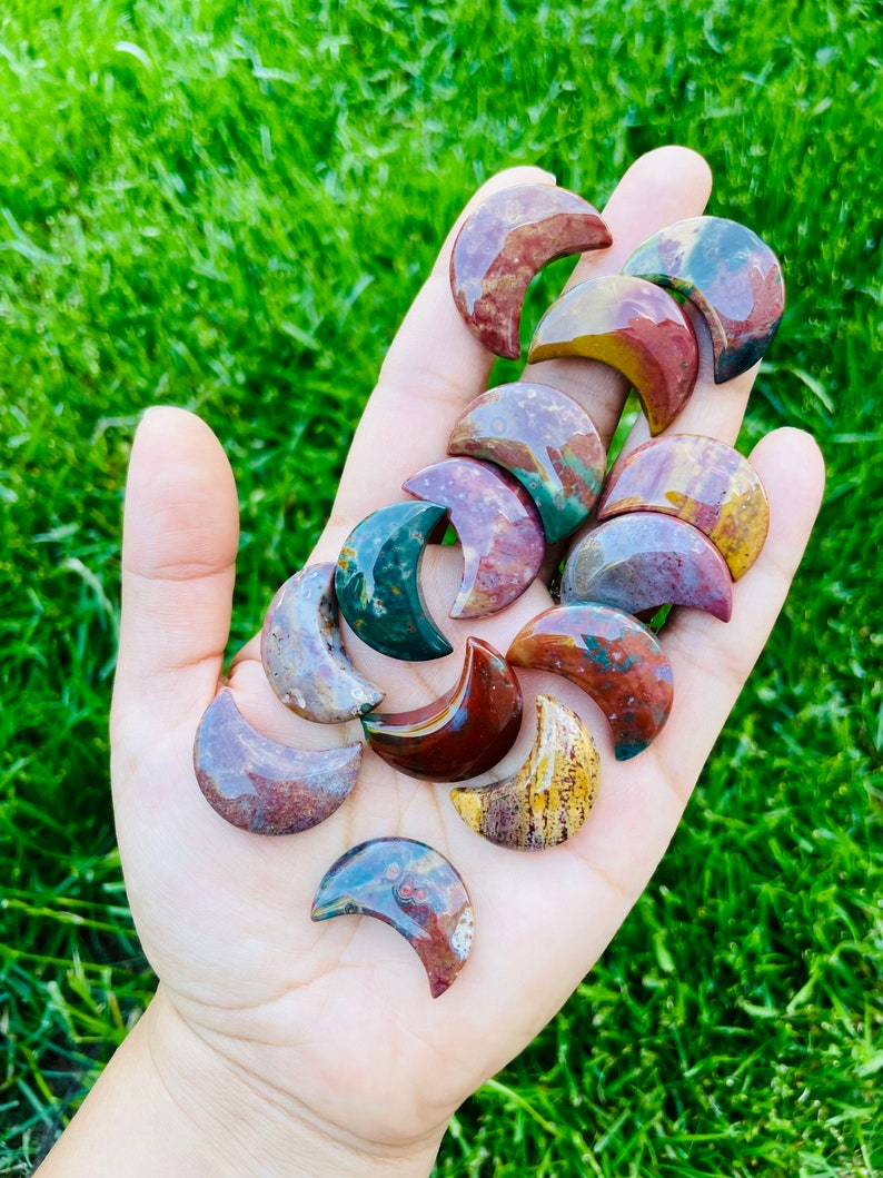 May include: A collection of polished, multi-colored, crescent moon shaped stones. The stones are a mix of red, brown, green, and yellow.