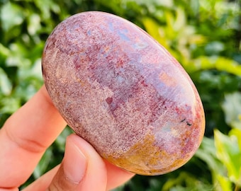 Può includere: Una pietra di diaspro rosso ovale, liscia e lucida, con macchie bianche e marroni. La pietra è tenuta in una mano.