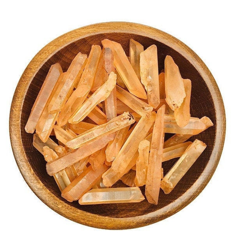 May include: A wooden bowl filled with a collection of orange quartz crystal points. The crystals are various sizes and shapes, with some being longer and thinner than others.