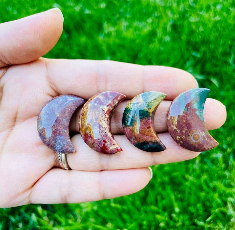 May include: Four crescent moon shaped polished stones with red, green, and brown patterns.