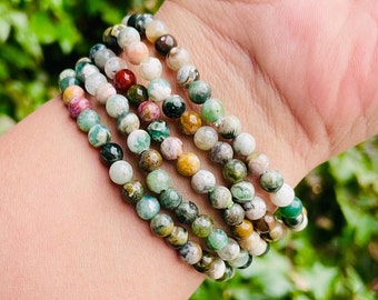 May include: A stack of five bracelets made with green, brown, and white jasper beads. The bracelets are stacked on a person's wrist.