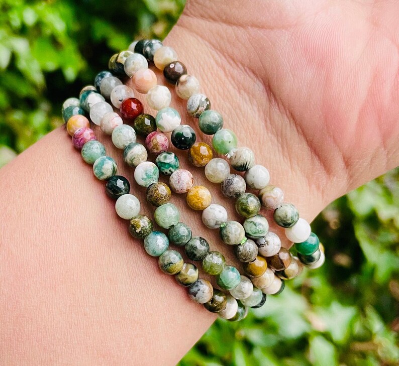 May include: A stack of five bracelets made with green, brown, and white jasper beads. The bracelets are stacked on a person's wrist.