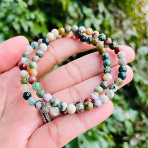 May include: A multi-colored gemstone bracelet with small, round beads. The bracelet is made of green, brown, red, and white stones.