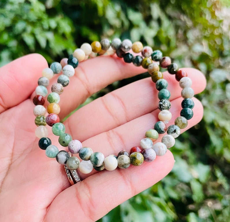 May include: A multi-colored gemstone bracelet with small, round beads. The bracelet is made of green, brown, red, and white stones.