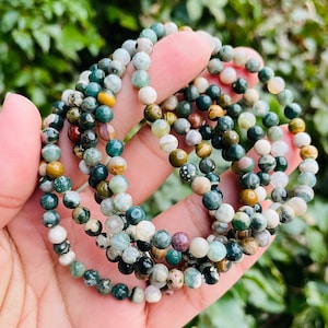 May include: A set of green, brown, and white gemstone bracelets. The bracelets are made of small, round beads and are stacked on top of each other.
