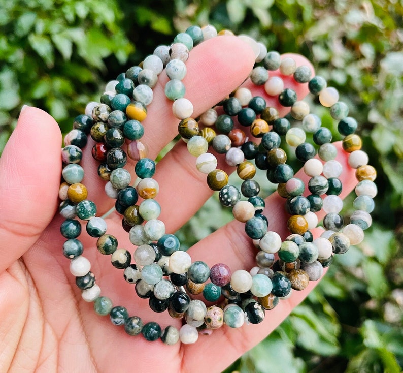 May include: A set of green, brown, and white gemstone bracelets. The bracelets are made of small, round beads and are stacked on top of each other.