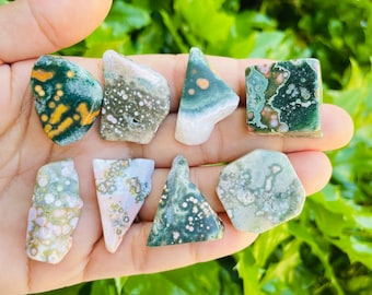 May include: A collection of eight green, white and pink ocean jasper tumbled stones. The stones are various shapes and sizes, and have a speckled pattern.