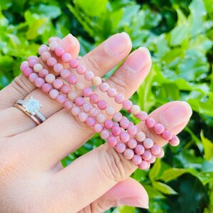 K&ouml;nnte beinhalten: Ein Stapel rosafarbener und wei&szlig;er Edelstein-Armb&auml;nder. Die Armb&auml;nder bestehen aus kleinen, runden Perlen und sind auf einem Gummiband aufgef&auml;delt.