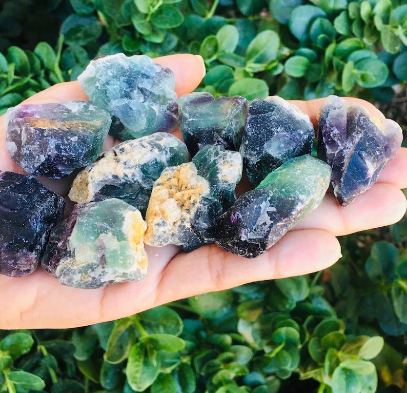 Pu&ograve; includere: Una collezione di cristalli di fluorite in varie tonalit&agrave; di verde, viola e nero. I cristalli sono grezzi e hanno un aspetto naturale non levigato.