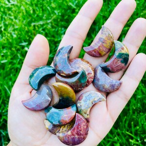 May include: A collection of ten polished, multi-colored, crescent moon shaped stones. The stones are a mix of red, green, brown, and white.