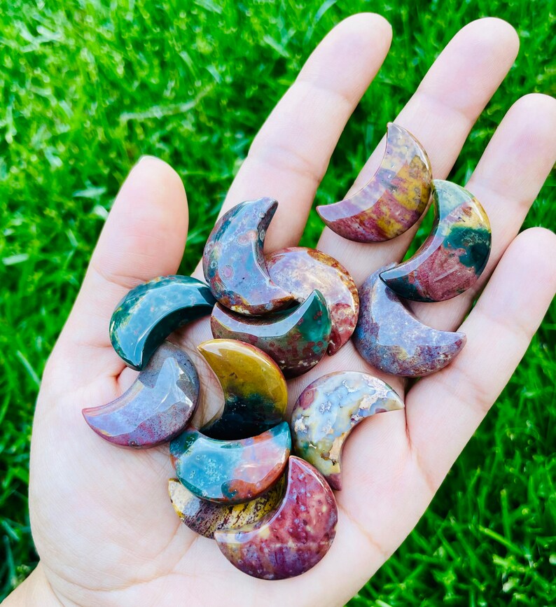 May include: A collection of ten polished, multi-colored, crescent moon shaped stones. The stones are a mix of red, green, brown, and white.