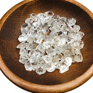 May include: A wooden bowl filled with a collection of clear quartz crystals. The crystals are rough and have a natural, unpolished look.