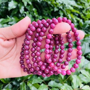 Puede incluir: Un conjunto de pulseras de piedras preciosas rosas con cuentas redondas. Las pulseras están hechas de cuentas de piedras preciosas rosas y están apiladas unas sobre otras.