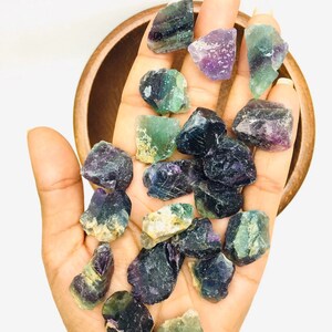 Pu&ograve; includere: Una collezione di cristalli di fluorite verde, viola e nero. I cristalli sono grezzi e hanno un aspetto naturale non lucidato.