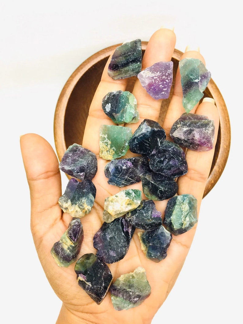 Pu&ograve; includere: Una collezione di cristalli di fluorite verde, viola e nero. I cristalli sono grezzi e hanno un aspetto naturale non lucidato.