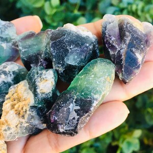 Pu&ograve; includere: Una collezione di cristalli di fluorite verdi, neri e viola. I cristalli sono grezzi e hanno una variet&agrave; di forme e dimensioni.