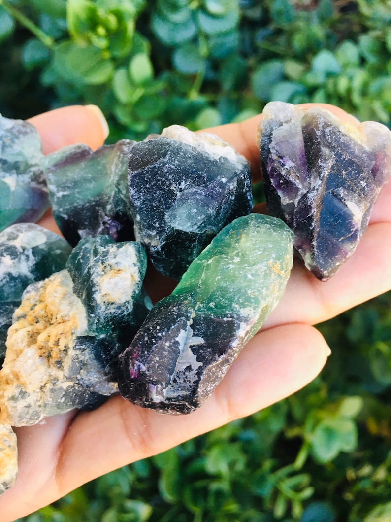 Pu&ograve; includere: Una collezione di cristalli di fluorite verdi, neri e viola. I cristalli sono grezzi e hanno una variet&agrave; di forme e dimensioni.
