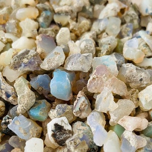 May include: A close-up of a pile of small, rough, white, and blue opal stones. The stones are various shapes and sizes, and some have a milky or iridescent appearance.