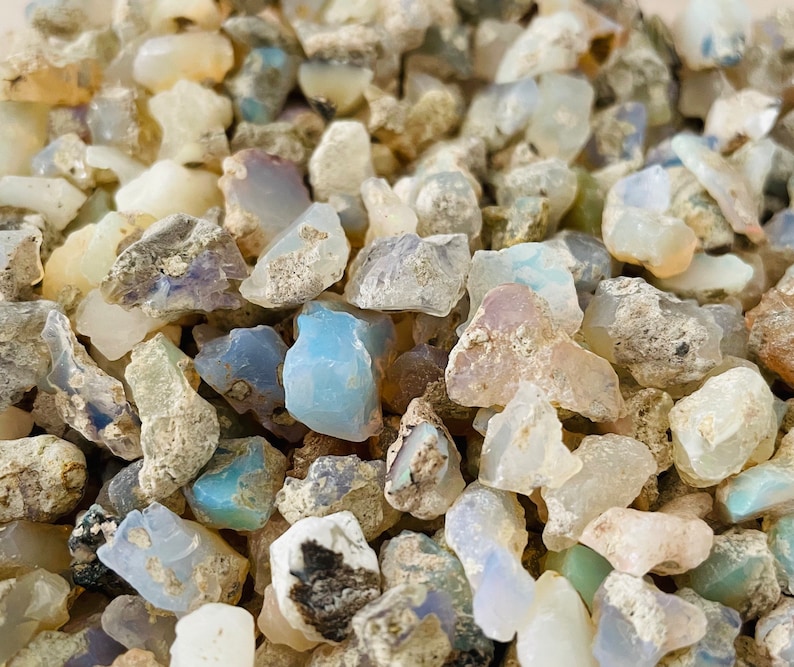 May include: A close-up of a pile of small, rough, white, and blue opal stones. The stones are various shapes and sizes, and some have a milky or iridescent appearance.