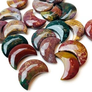 May include: A collection of polished, crescent-shaped stones in shades of red, green, and brown. The stones are made of a variety of materials, including agate and jasper.