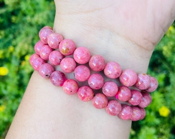 May include: A pink gemstone bracelet with multiple strands of round beads. The bracelet is made of pink rhodonite stones.
