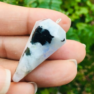 Może przedstawiać: Wisiorek z białego, czarnego i niebieskiego kryształu z srebrną zawieszką. Kryształ jest naturalnym kamieniem o spiczastym kształcie.