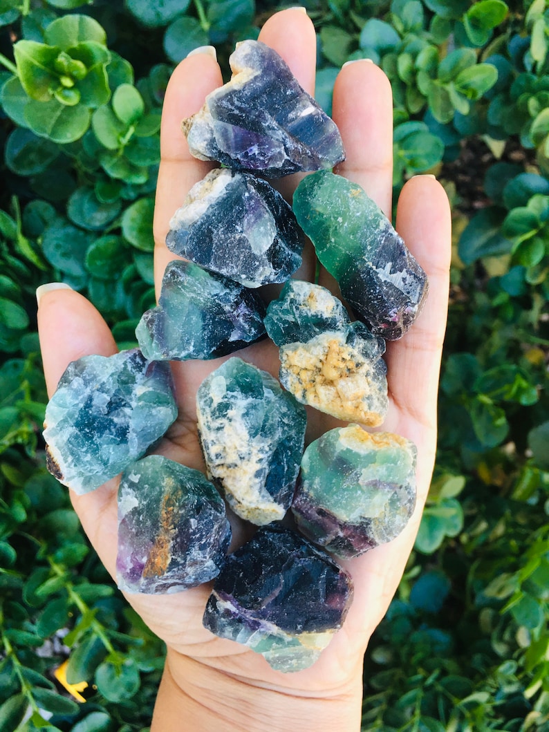 Pu&ograve; includere: Una collezione di cristalli di fluorite verdi, viola e bianchi. I cristalli sono grezzi e hanno un aspetto naturale non levigato.