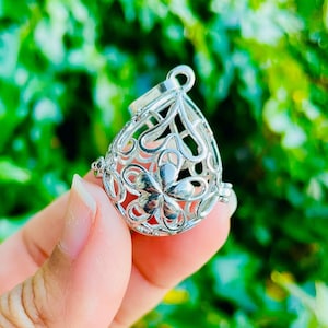 May include: A silver charm with a delicate floral design. The charm is shaped like a teardrop and has a small loop at the top for attaching to a necklace or bracelet.