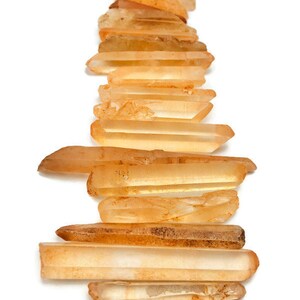 May include: A collection of 15 orange quartz crystal points, also known as citrine, arranged in a vertical stack. The points are various sizes and shapes, with some being more translucent than others.