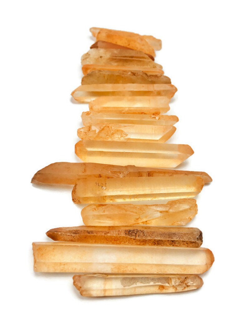 May include: A collection of 15 orange quartz crystal points, also known as citrine, arranged in a vertical stack. The points are various sizes and shapes, with some being more translucent than others.
