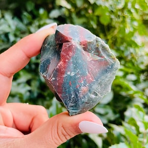 May include: A rough, natural, green, red, and black bloodstone crystal. The crystal is irregularly shaped and has a smooth, polished surface.