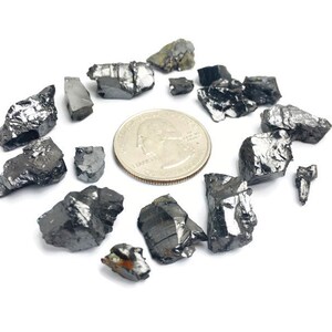 May include: A collection of black, irregularly shaped, rough-textured stones, some with a metallic sheen, scattered around a silver US quarter.